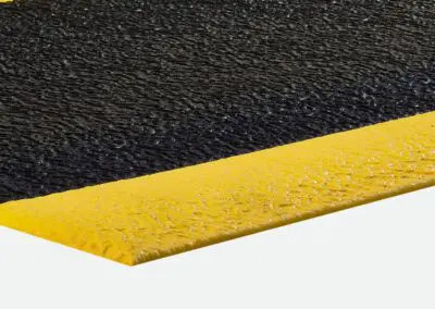 A close-up of black textured safety matting with yellow edges to it.