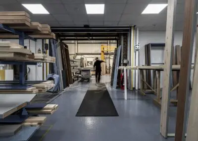 A long run of black textured safety mat in a workshop that has multiple racks of freshly sawn timber on it.