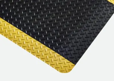 A close-up of black checker-plate textured safety matting with yellow edges.