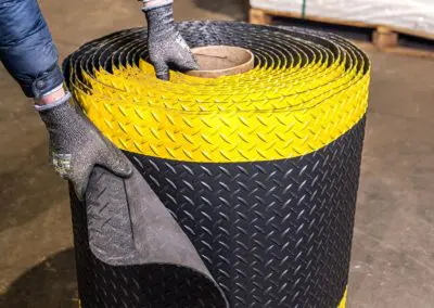 A roll of black checker-plate textured safety matting with a yellow edge on it.
