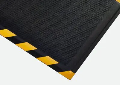 A black safety mat with a dotted surface and yellow and black hashing down one side