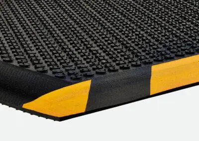 A black safety mat with a dotted surface and yellow and black hashing down one side.