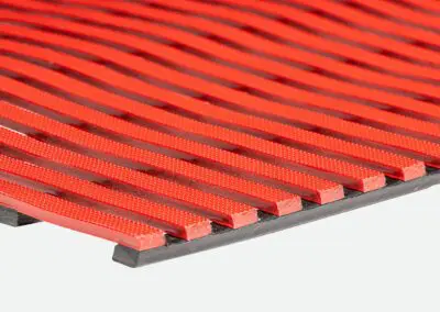 A close up of a red safety mat with regular rectangular holes.
