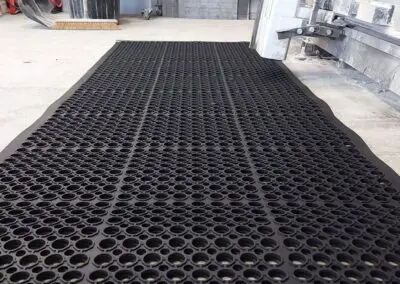 A safety mat with regular circular holes in it in from of some industrial equipment.
