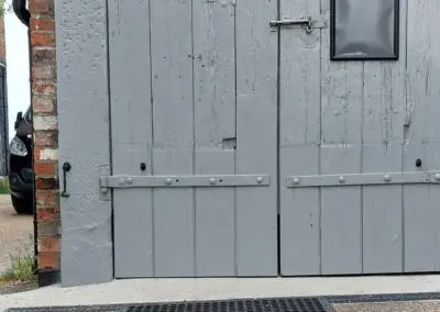 A safety mat with regular circular holes in it in front of a pair of wooden doors.
