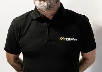 A shot of a middle-aged, bald man in a black Morgan Rushworth Polo Shirt.