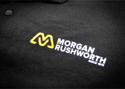 A close-up of the logo on a black Morgan Rushworth polo shirt
